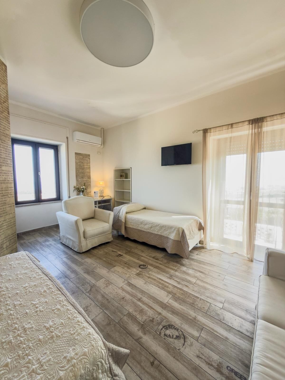 A room with a sofa, two single beds, a chair, a TV, and a window with curtains.
