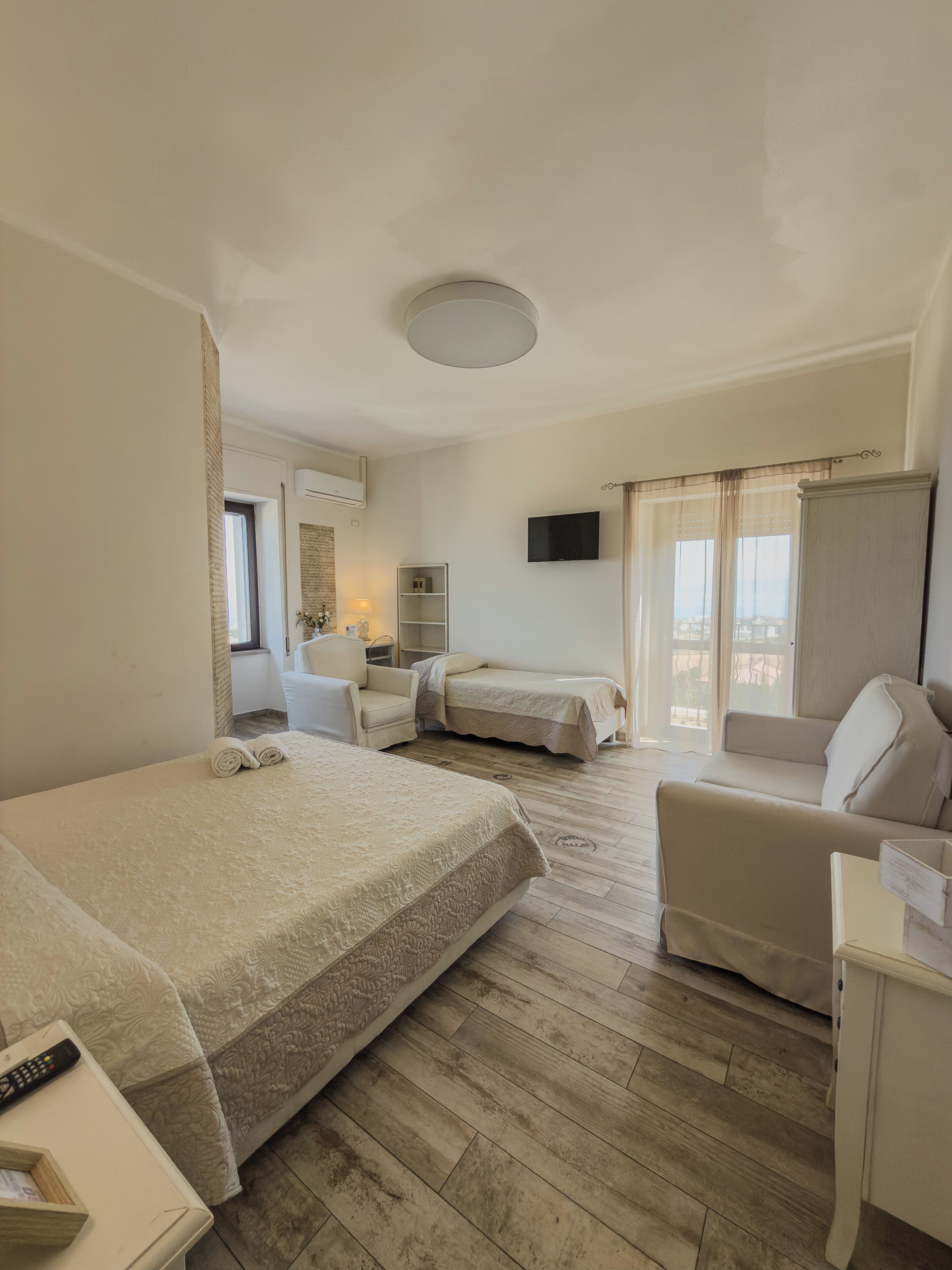 Une chambre d’hôtel avec un grand lit, un lit plus petit, un canapé, une télévision et une fenêtre avec des rideaux.