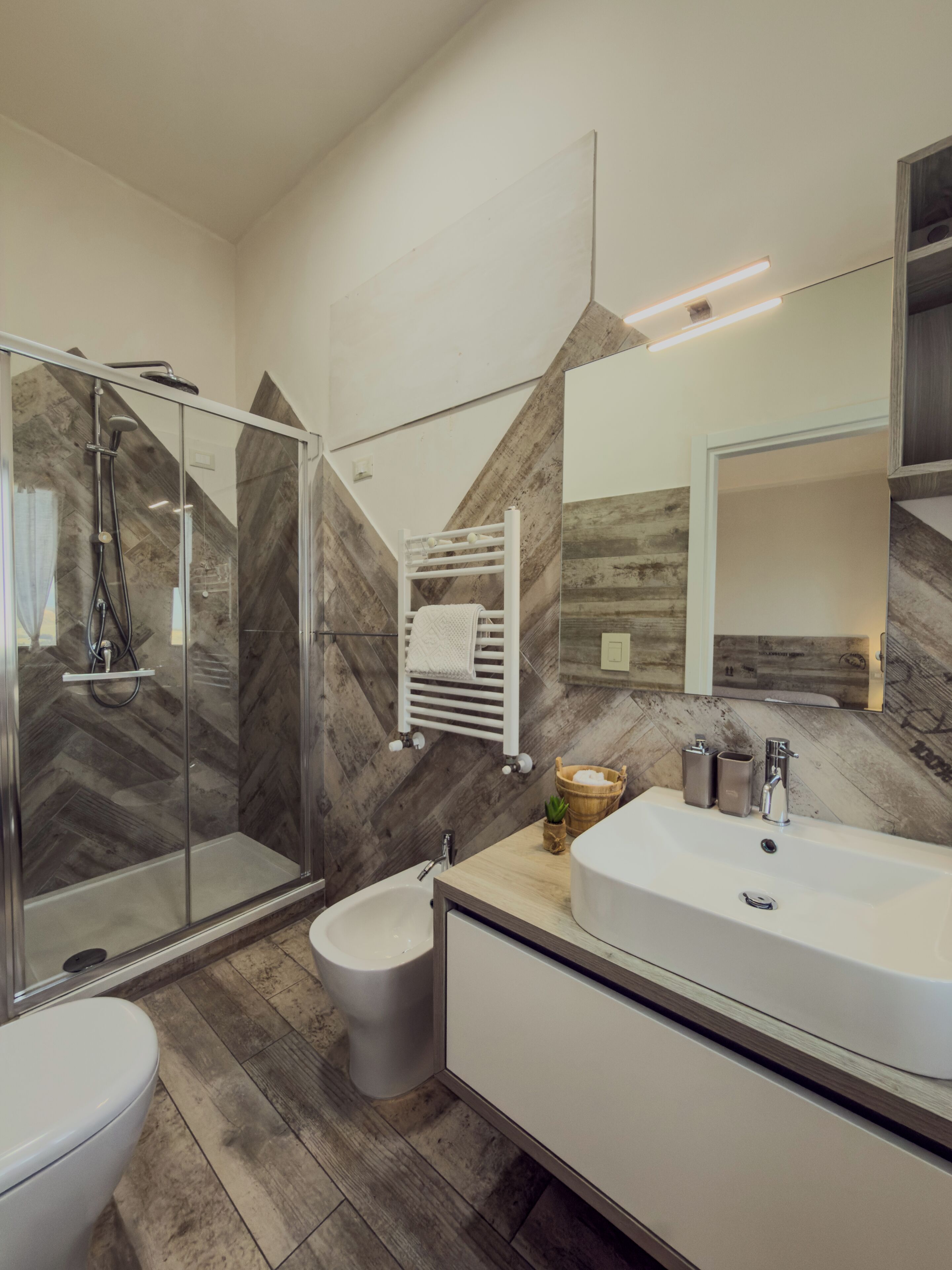 Une salle de bain moderne avec une douche à l’italienne en verre, des toilettes blanches, un bidet et un meuble-lavabo avec un miroir.