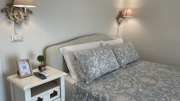 Un letto rifatto con lenzuola a fantasia, un comodino con telecomando e un cartello, e lampade a parete.