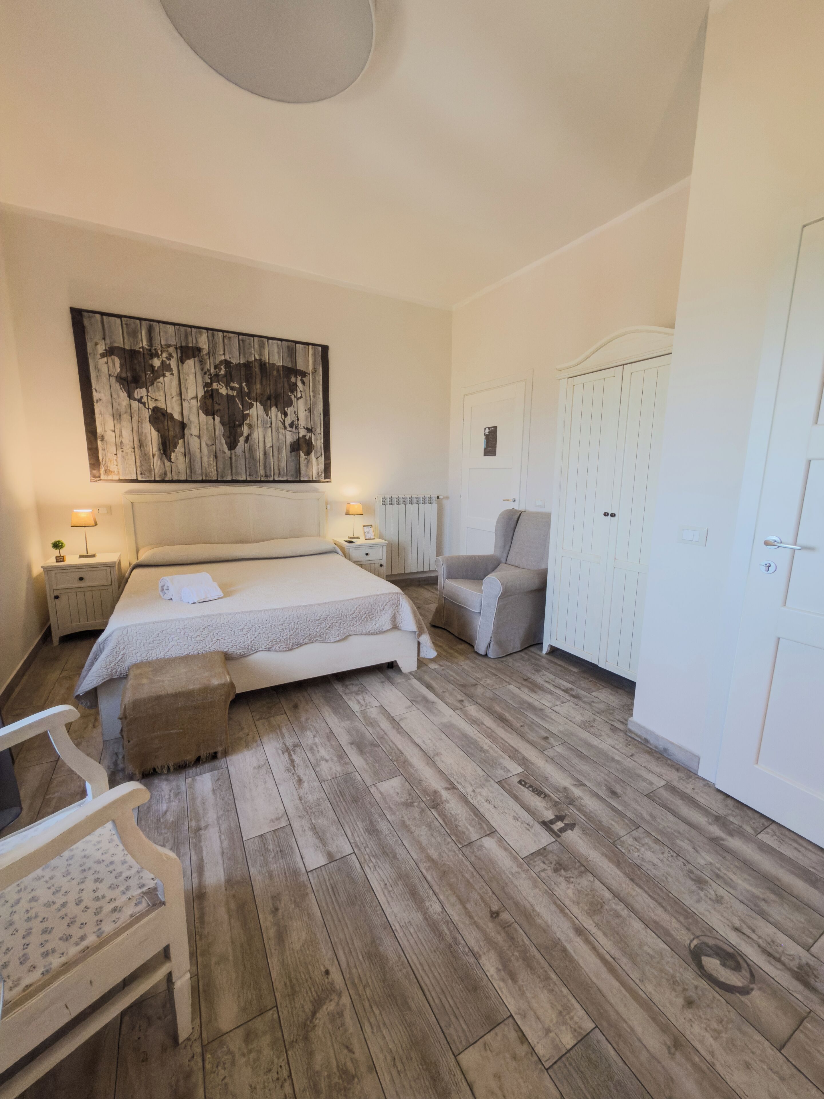 A bedroom with a bed, a chair, a wardrobe, and a world map on the wall.