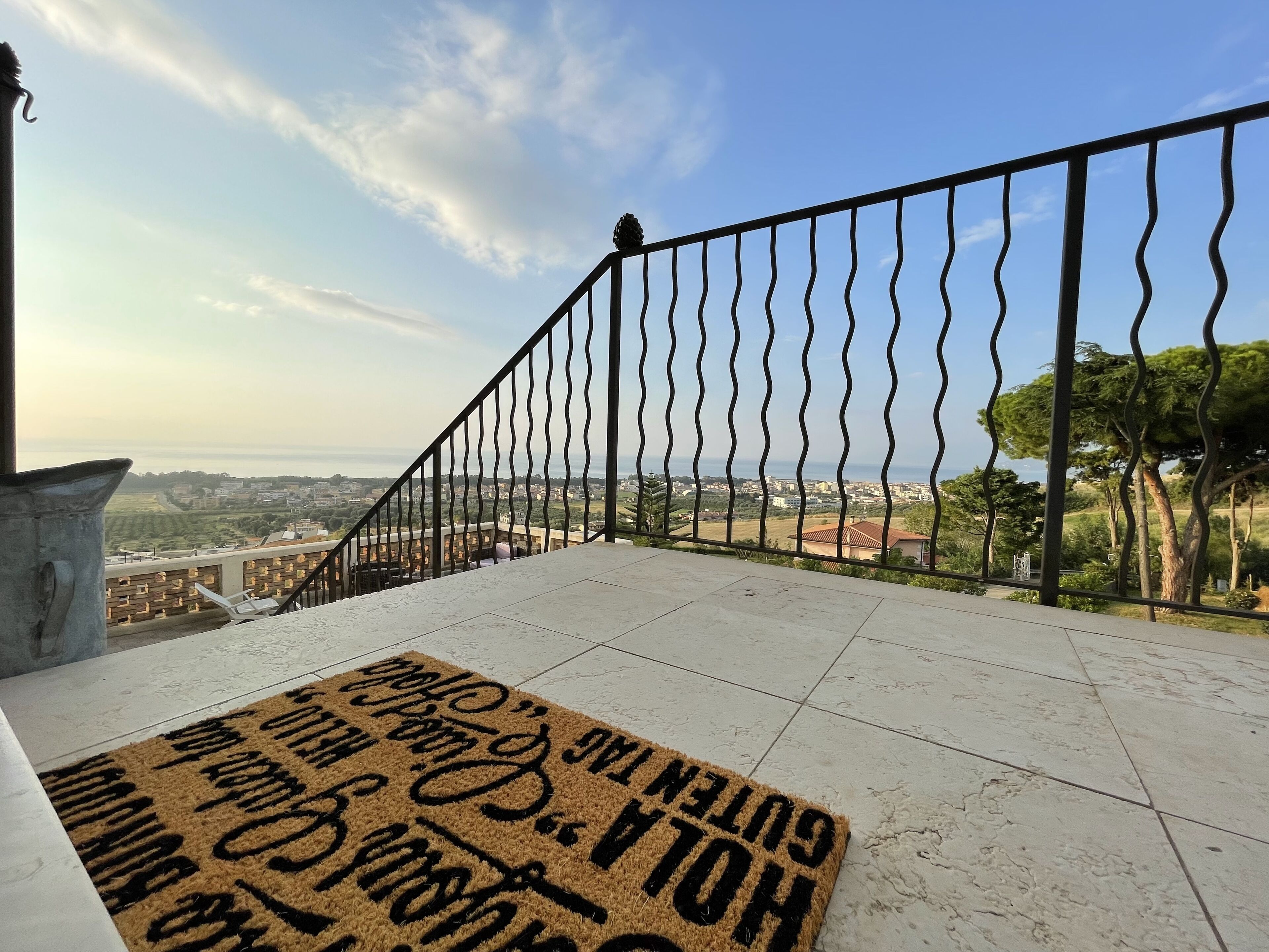 Un balcón con vistas a un paisaje urbano, un felpudo con texto y una barandilla metálica.