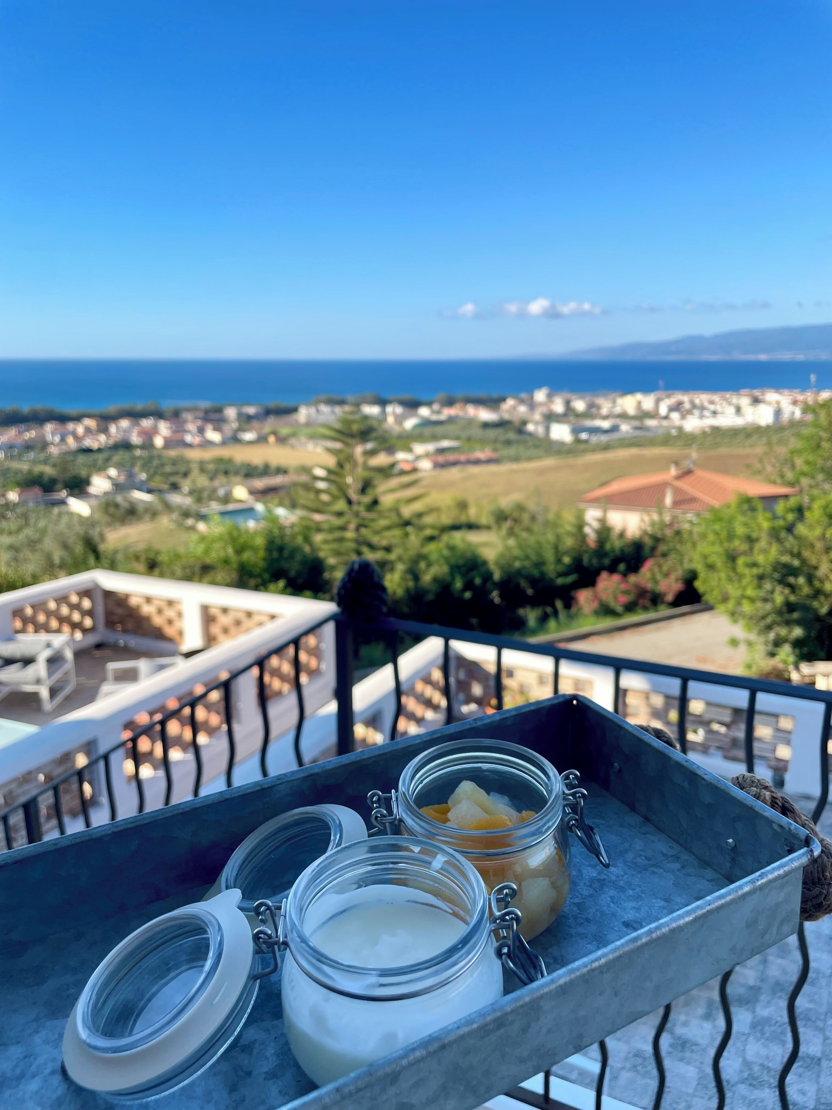 Un balcone con un vassoio che porta barattoli di cibo e vista sul mare e sulla città.