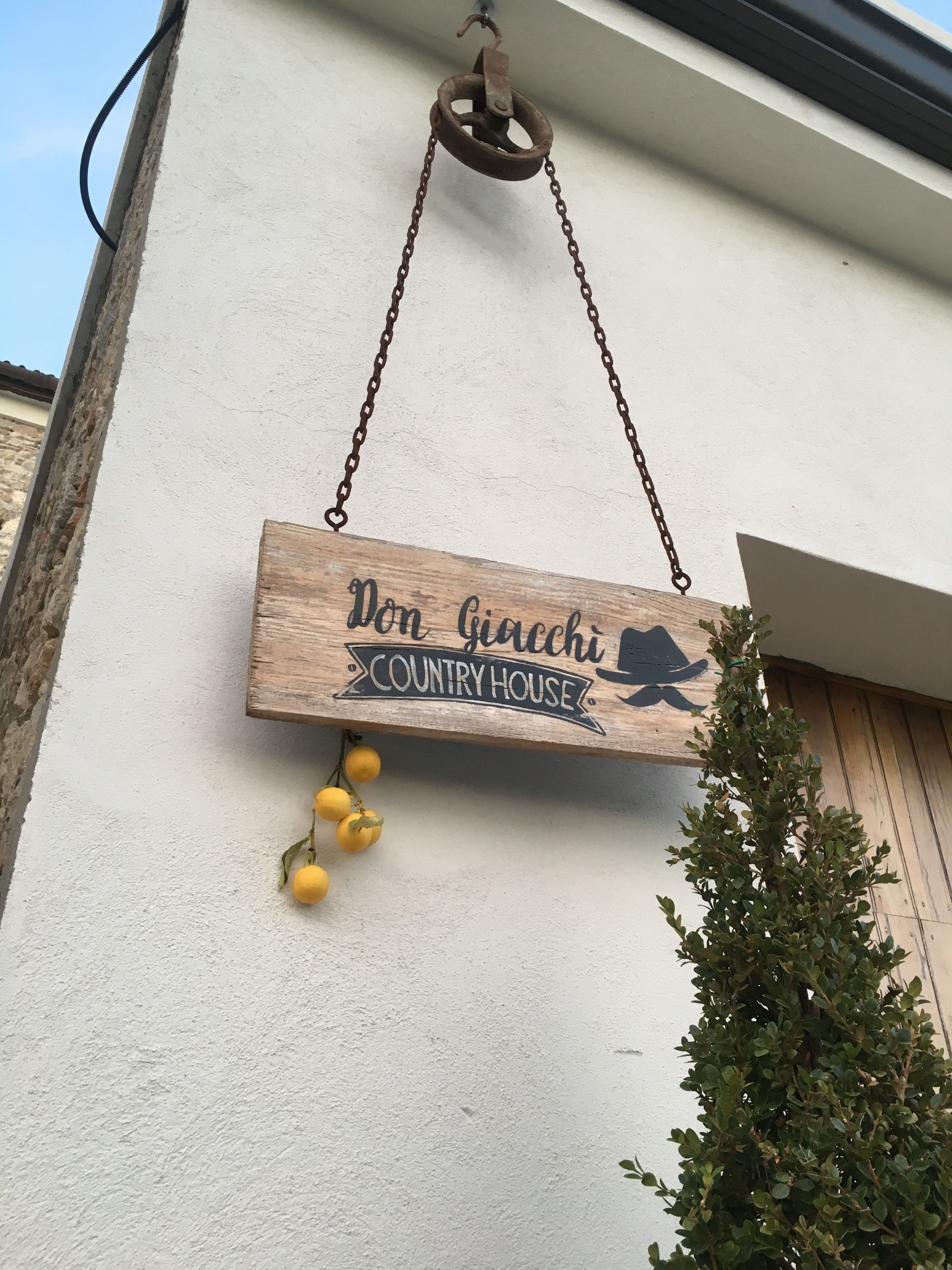 A wooden sign with the text "Don Giacchi COUNTRY HOUSE" hanging from a chain.