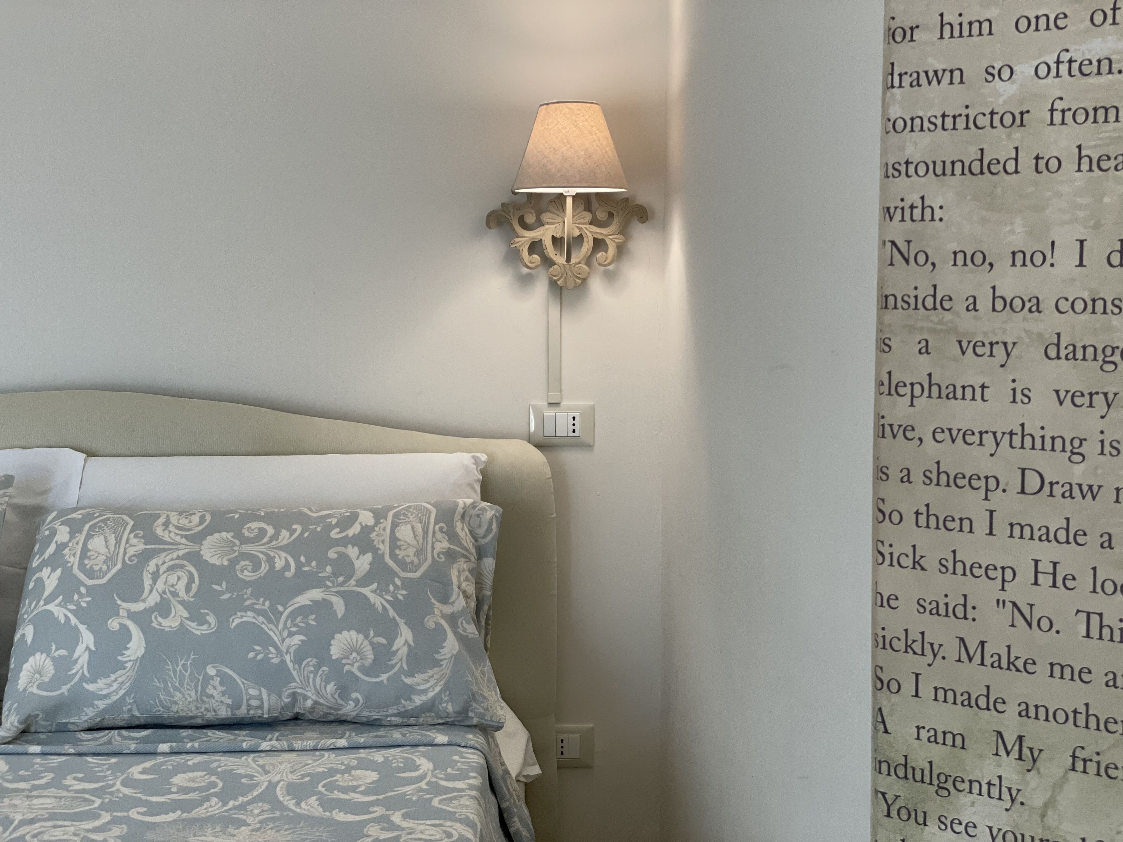A bedroom with a bed, a wall-mounted lamp, and a wall with text.