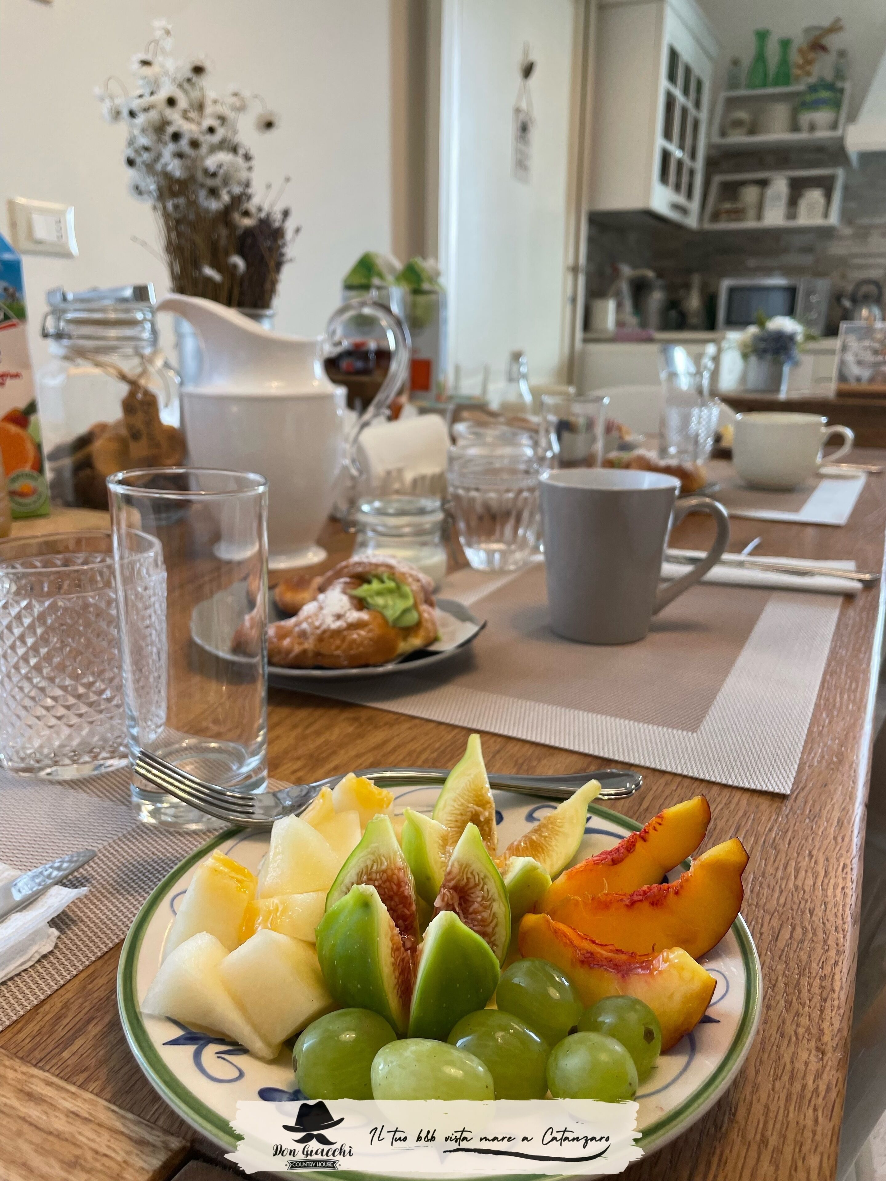 Una mesa de desayuno con un plato de fruta, una jarra y una taza.
