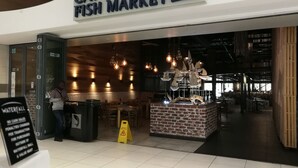 La entrada del Mercado de Pescado de Ciudad del Cabo, con un cartel sobre la puerta, un letrero de piso mojado y un aviso de que no se aceptan efectivo.