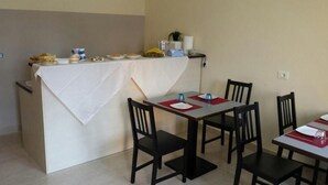 Ein Essbereich mit einem Tisch für vier Personen, Stühlen, einem Büfett mit Speisen und einer kleinen Pflanze auf einem Regal.