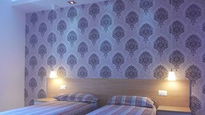 Ein Zimmer mit zwei Betten, gemustertem Wandpapier und Nachttischlampen.