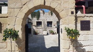An entrance with a stone archway leading to a building with a stone facade, potted plants, and a sign indicating a house of worship. - Salento Ada's House (Melendugno)