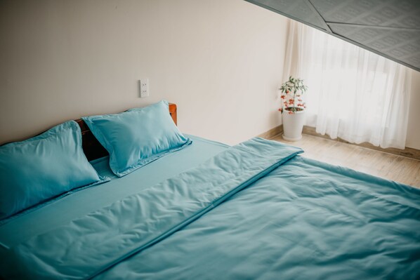 A bedroom with a bed, pillows, a potted plant, and a window with curtains. - Le Phuong BB (Xuan Huong - Da Lat)