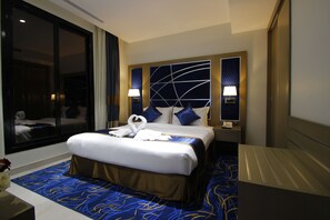 A hotel room with a large bed, two bedside lamps, a headboard with a geometric design, and a view of another room through a sliding door.