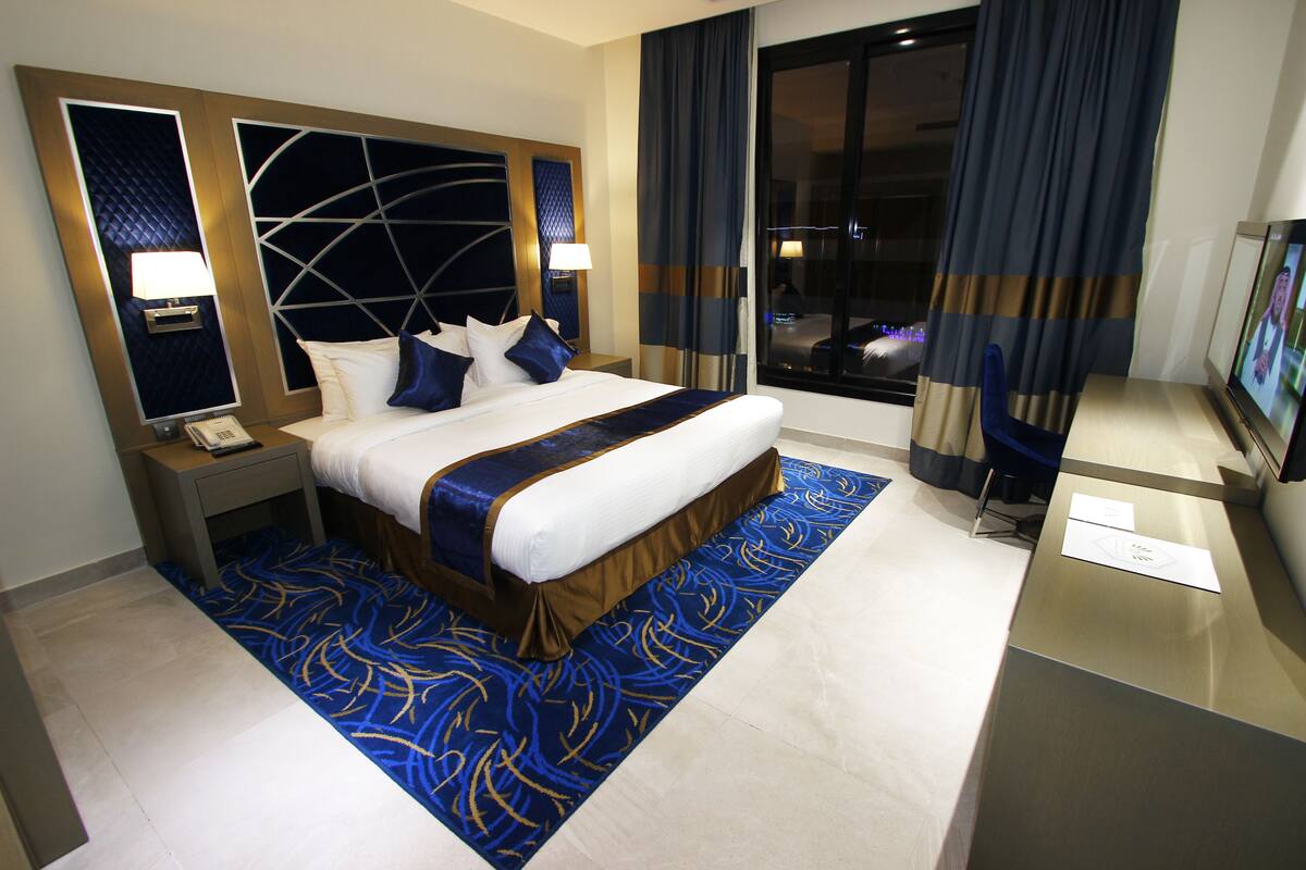 A hotel room with a large bed, a desk, a TV, and a view of the city at night.