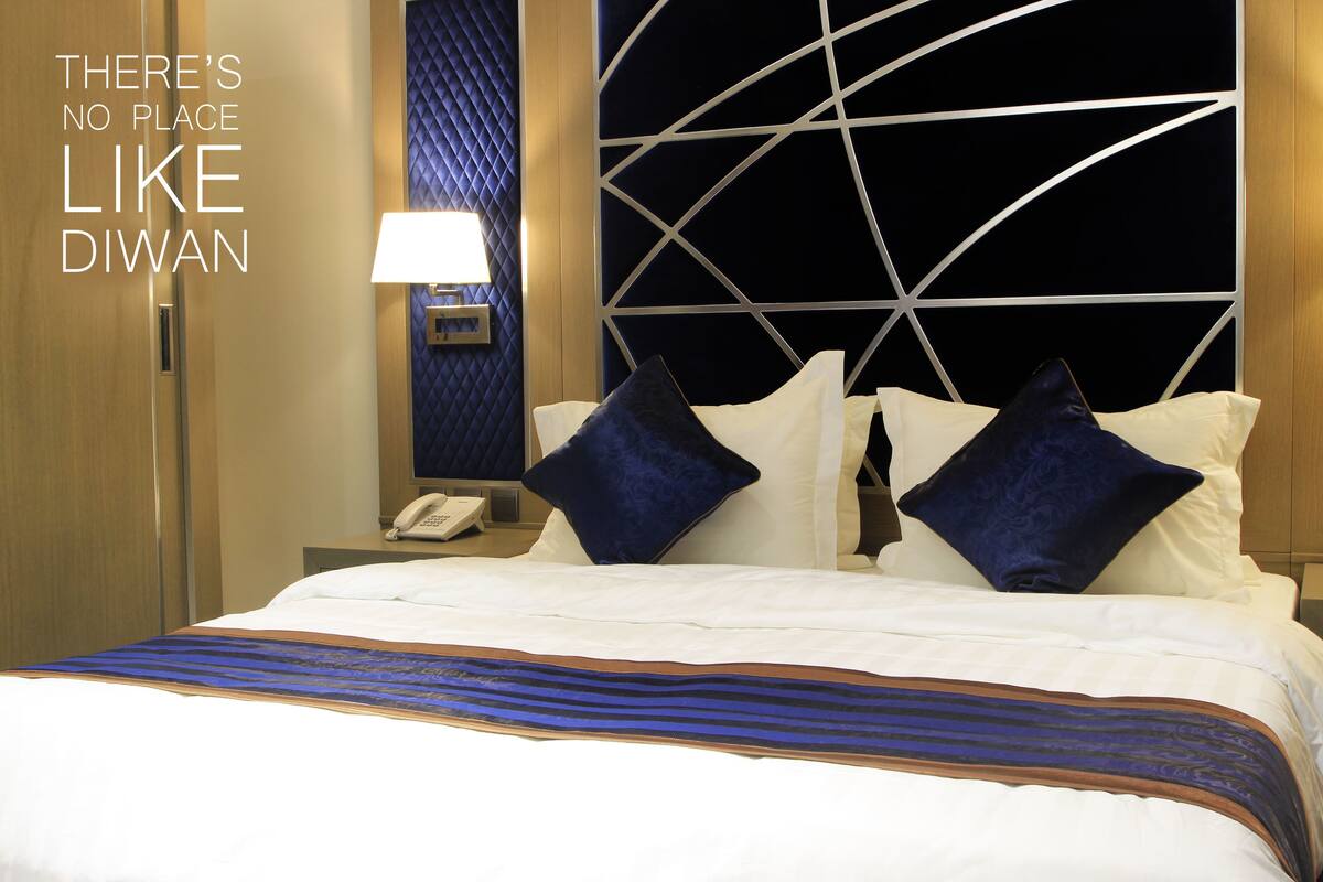 A hotel room with a bed, a nightstand with a lamp, and a wall with a geometric pattern.