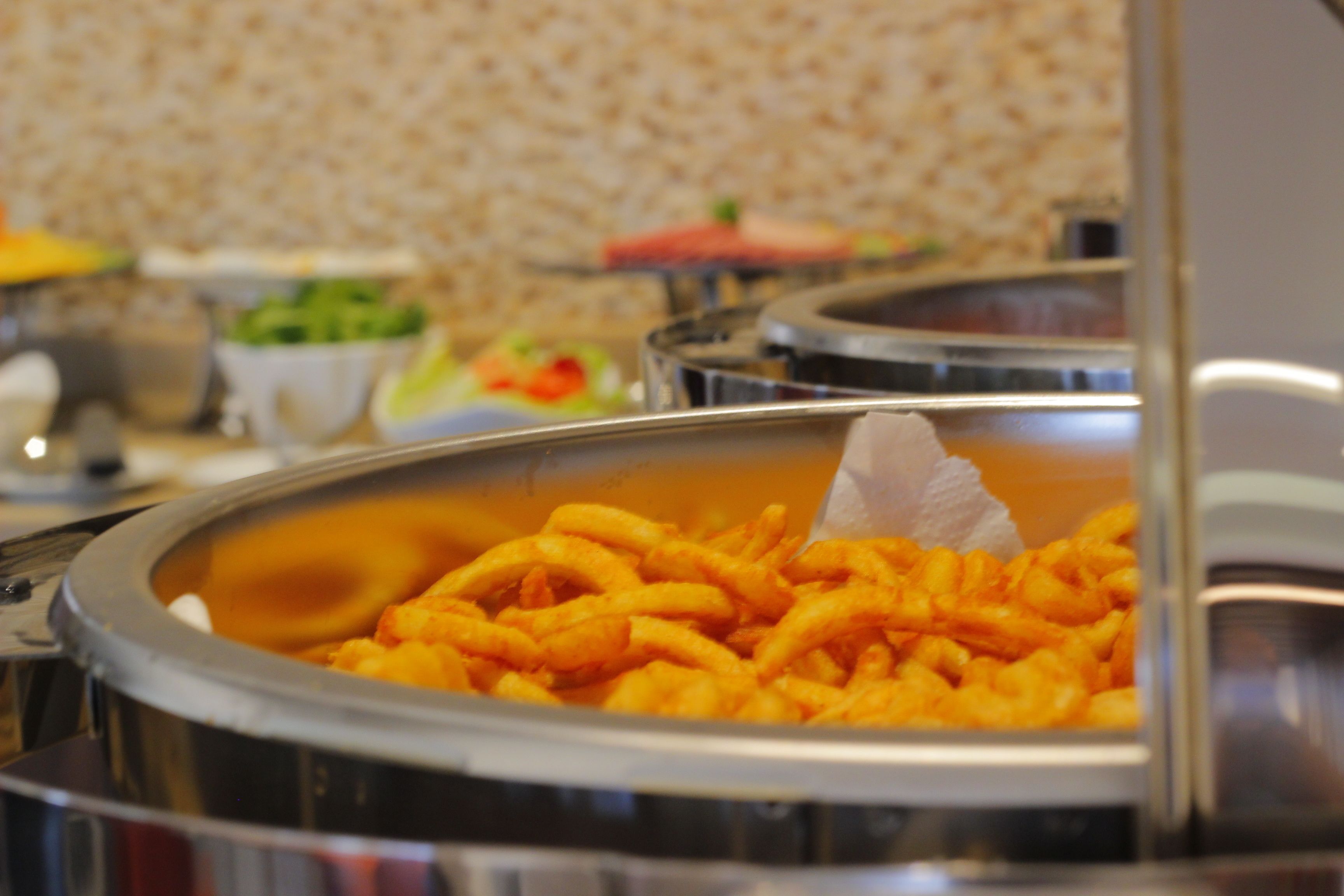 Un bufé con varios alimentos, incluyendo un recipiente grande de comida anaranjada, posiblemente frita, y otros platos al fondo.