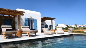 A poolside area with lounge chairs and a pergola. - Livadi House Mykonos (Mykonos)