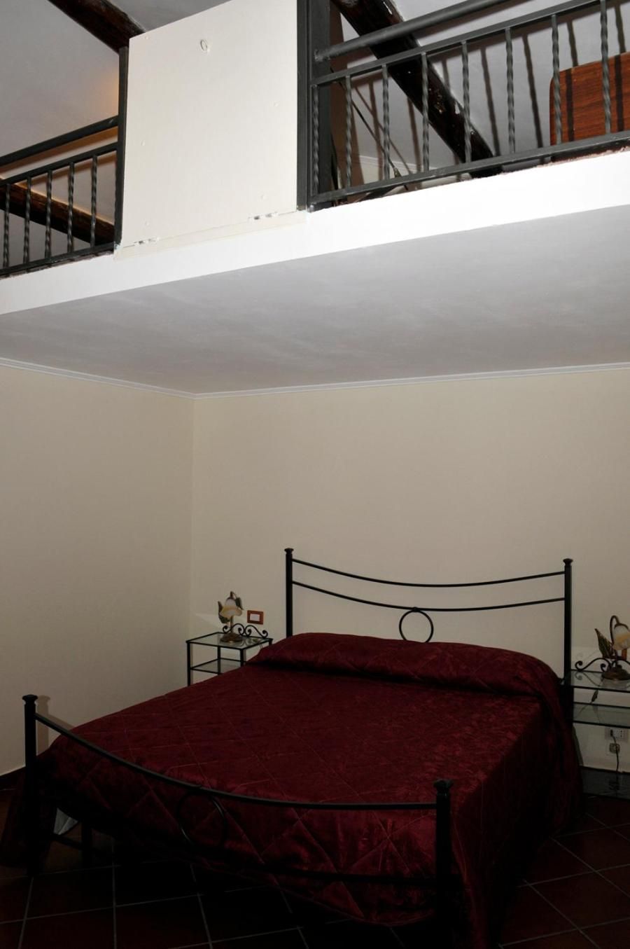Una habitación con una cama, una mesita de noche con lámpara y una escalera.