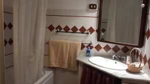 Un baño con bañera, lavamanos, espejo y toallero.