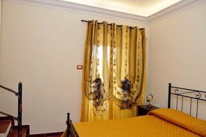 Un dormitorio con cama, mesita de noche, lámpara y ventana con cortinas.