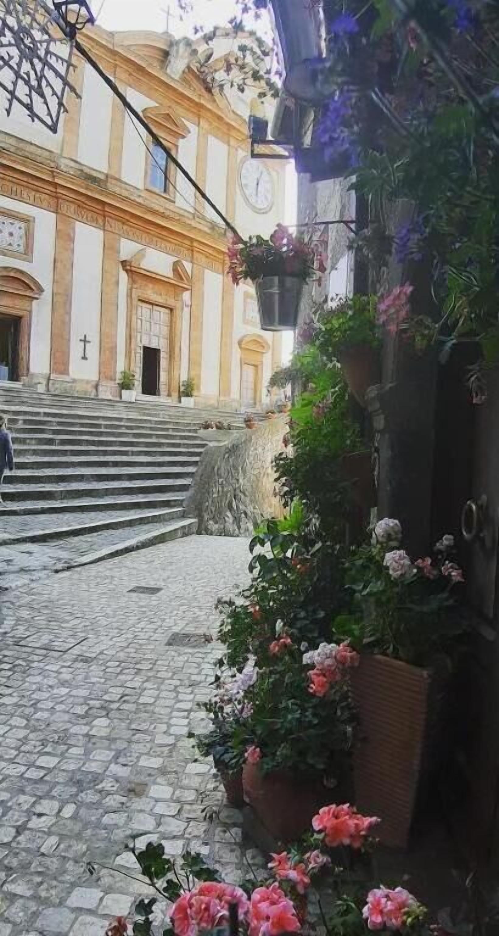 Una calle empedrada que conduce a un edificio con un reloj y una cruz en la fachada.