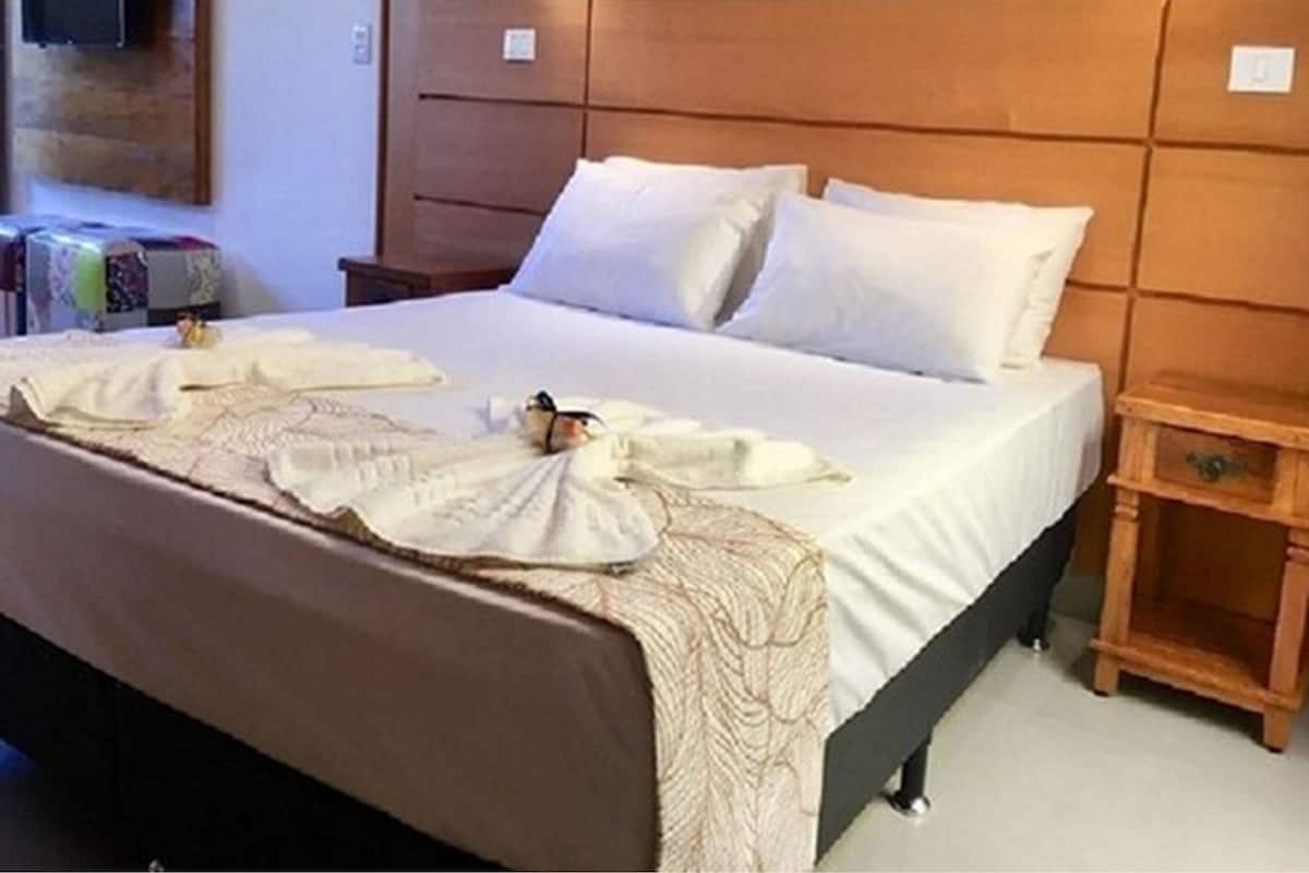 A neatly made bed with a headboard, a bedside table, and a wall-mounted TV.