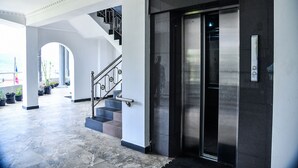 Entrada moderna de un edificio con escaleras, ascensor y plantas en macetas.