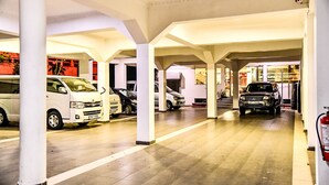 Un área de estacionamiento techada con varios coches aparcados bajo pilares blancos.