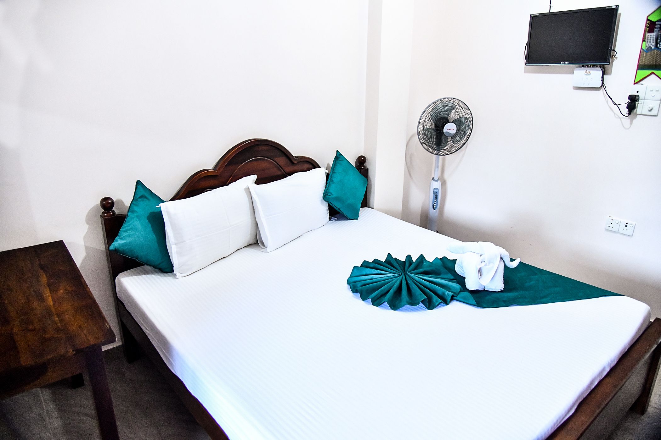 A neatly made bed with white and teal pillows, a wooden headboard, and a teal decorative pillow on the bed.