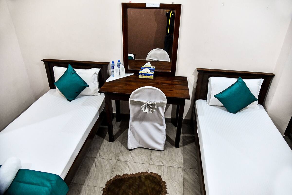 A small, clean room with two single beds, a wooden table, and a mirror.