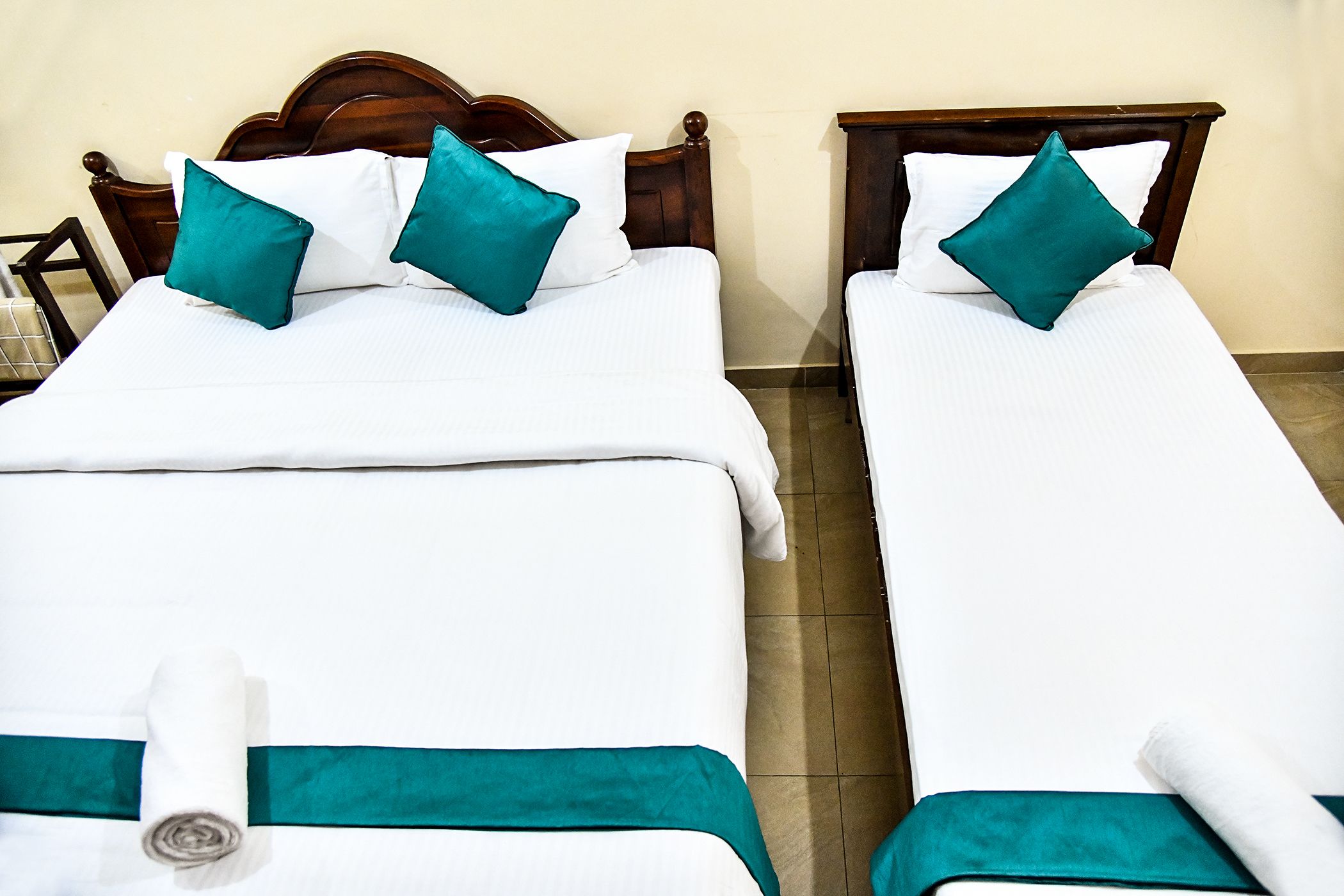 Deux lits simples avec des têtes de lit en bois, du linge de lit blanc et des oreillers de couleur turquoise.