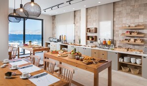 A modern kitchen with a breakfast buffet, wooden furniture, and a view of the sea. - Carian Hotel (Kalymnos)