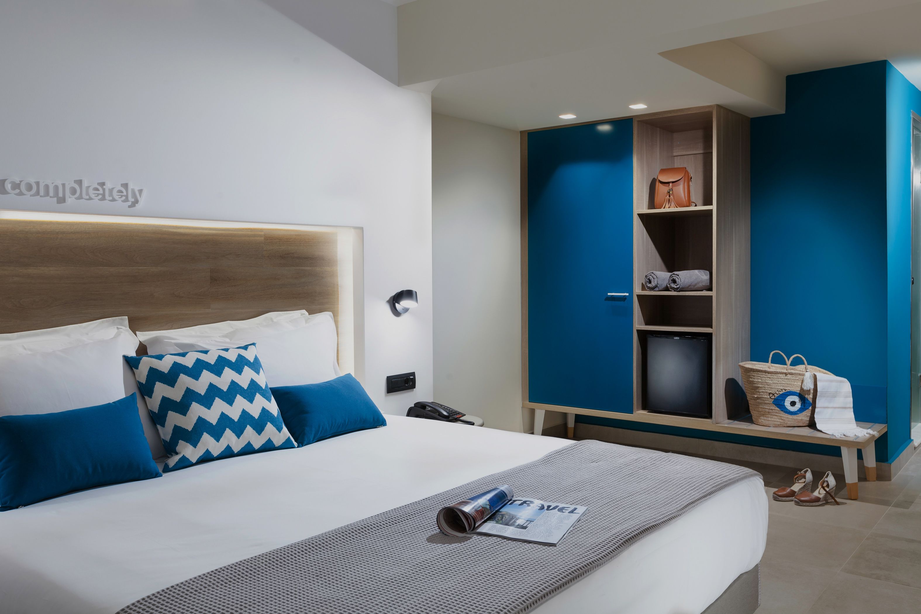 Une chambre d’hôtel avec un lit bien fait, une grande armoire et un banc sur lequel sont posés un sac à main et des chaussures.