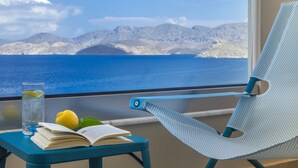 Un balcón con vista al mar, una silla, una mesa con un libro y un vaso de agua, y un limón.