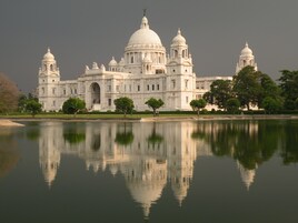 Un edificio grande, blanco e histórico con múltiples cúpulas y ventanas de arco, reflejado en aguas tranquilas.