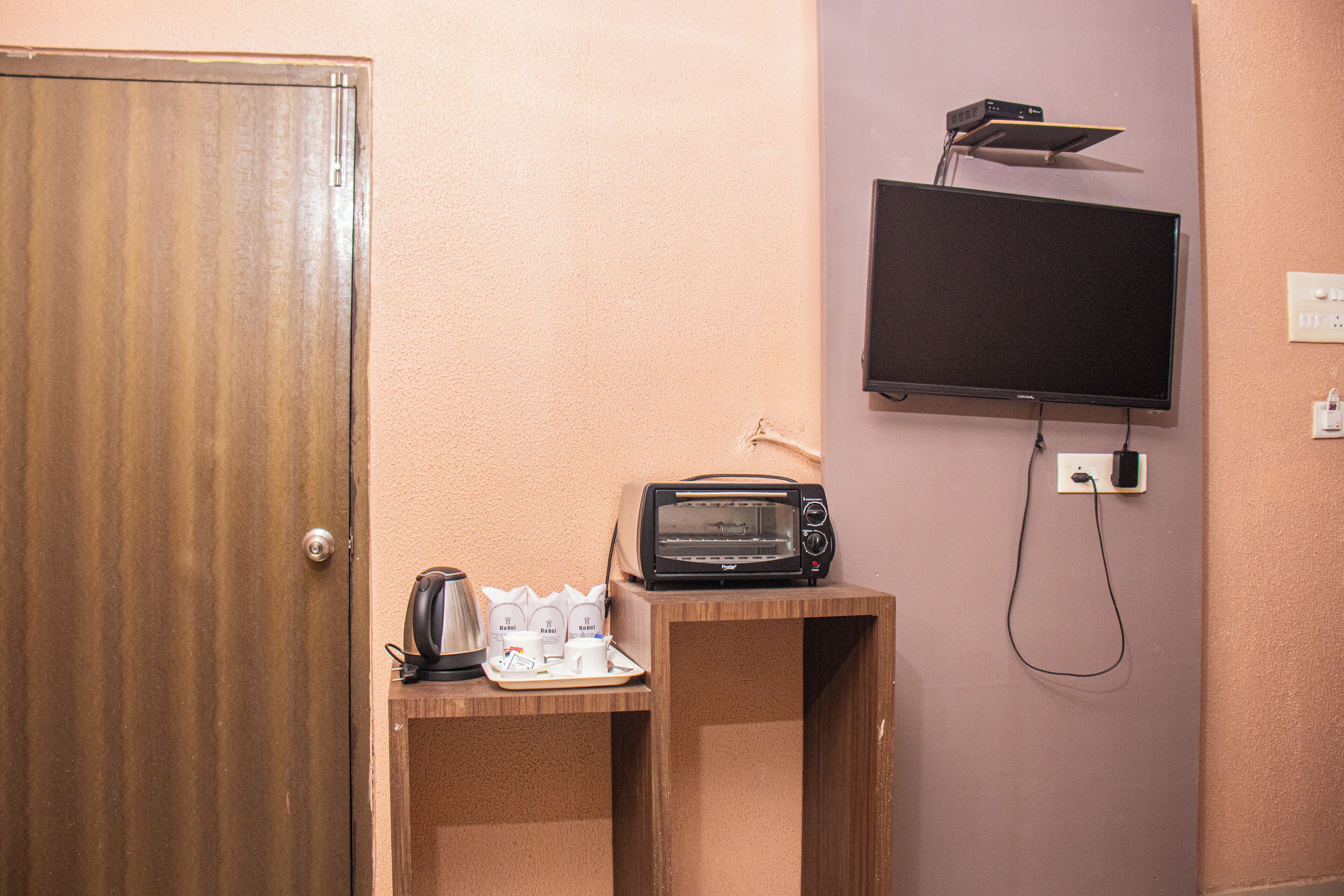 A room with a wooden door, a small wooden table with a toaster, a kettle, and a tray of cups and a coffee pot.
