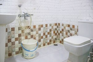 Baño con lavamanos blanco, inodoro y ducha. Hay un cubo en el suelo.