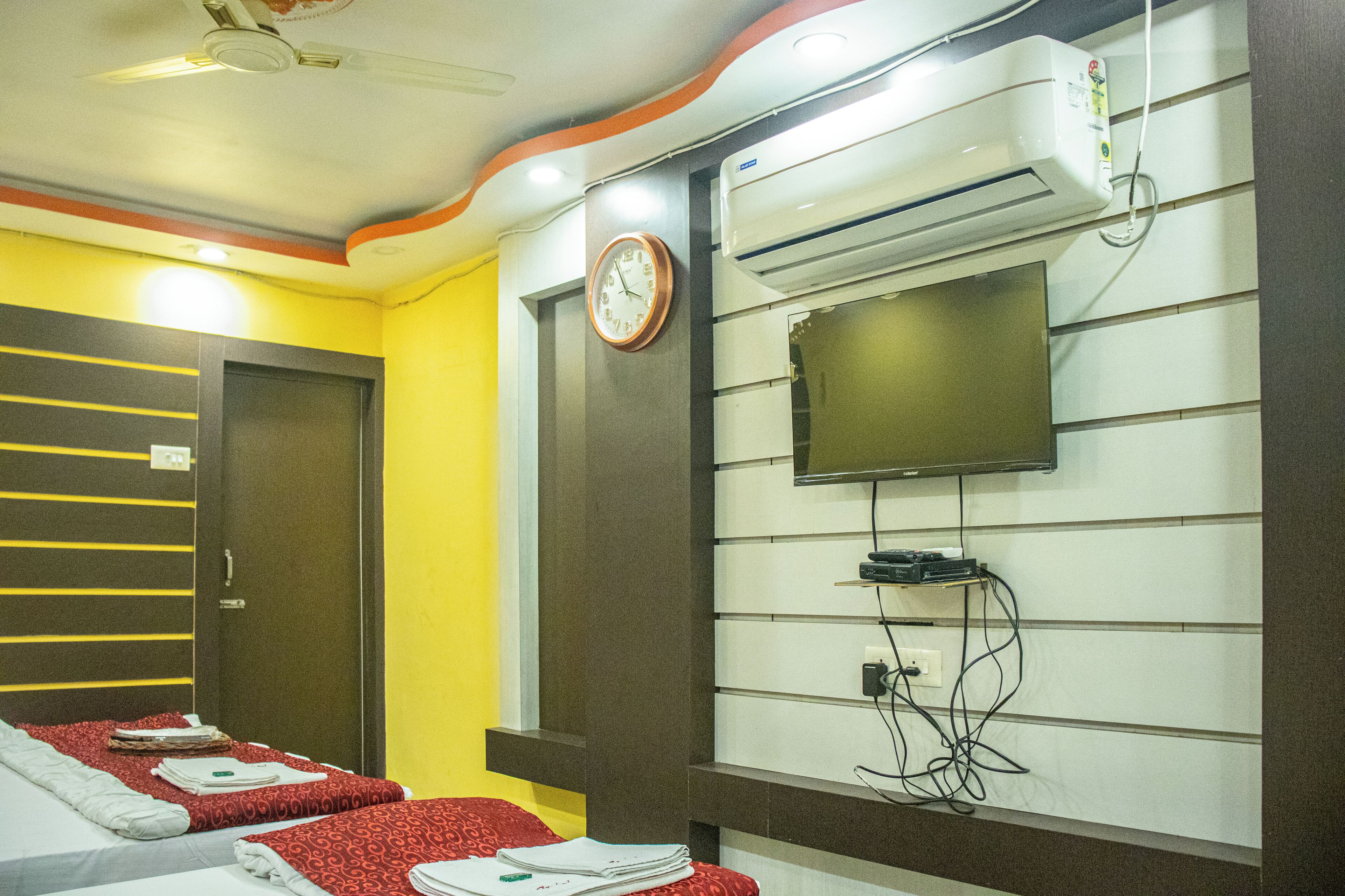 Habitación de hotel con cama, un reloj, equipo de aire acondicionado y televisor montado en la pared.