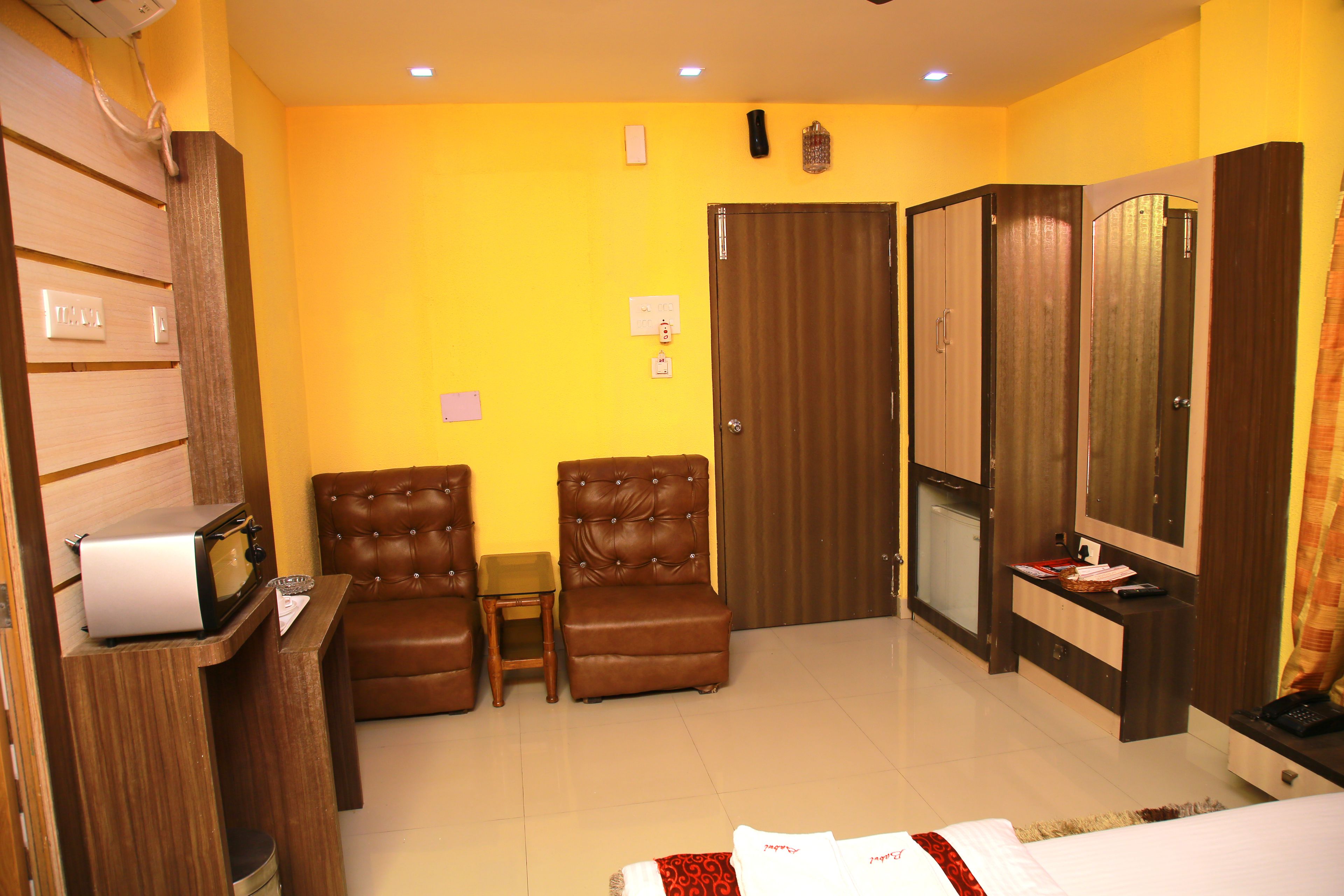 Habitación de hotel con cama, escritorio con microondas, dos sillones de cuero, una mesita, armario y espejo.