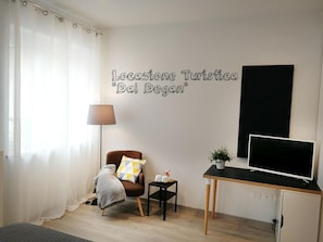 A modern room with a bed, a chair with a blanket, a small table with a plant, a lamp, and a TV on a stand. - Locazione Turistica Dal Degan (San Bonifacio)
