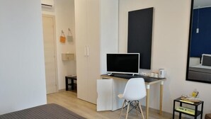 A modern hotel room with a bed, a desk with a computer, a chair, a small table, and a mirror. - Locazione Turistica Dal Degan (San Bonifacio)
