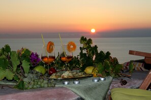A table set with food and drinks, a sunset in the background, and a view of the sea. - Agriturismo Zibibbodoro (Pantelleria)