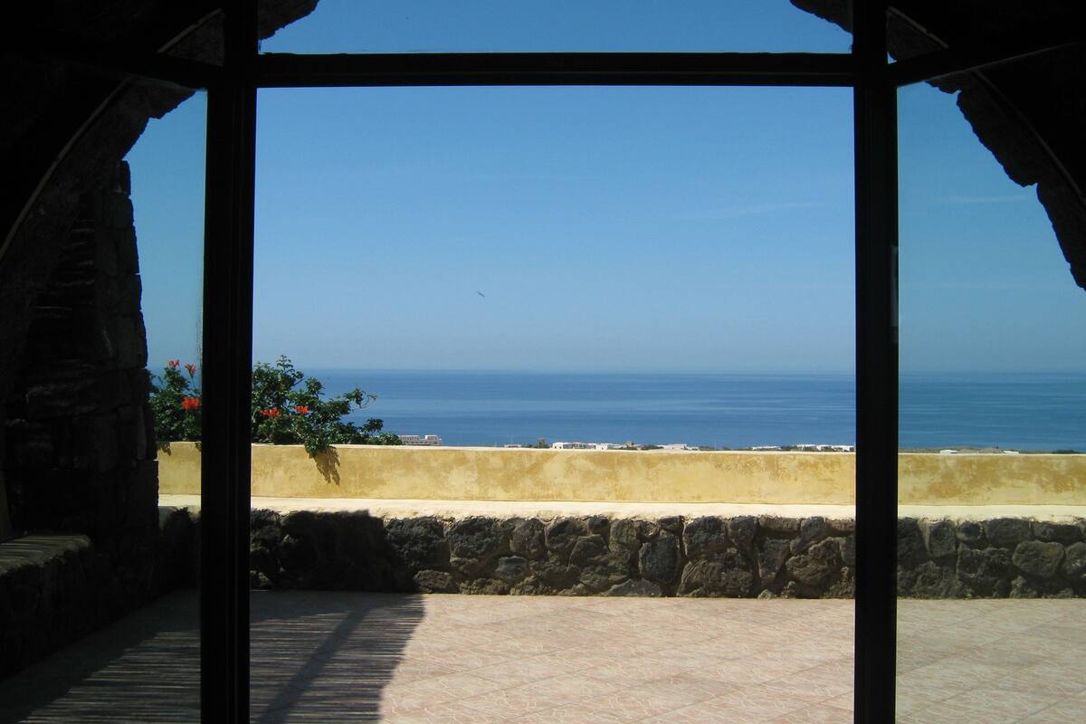 An arched doorway leading to a terrace with a view of the sea.
