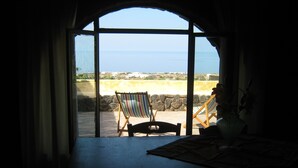 A room with a large arched window overlooking a beach with a striped beach chair and a table.