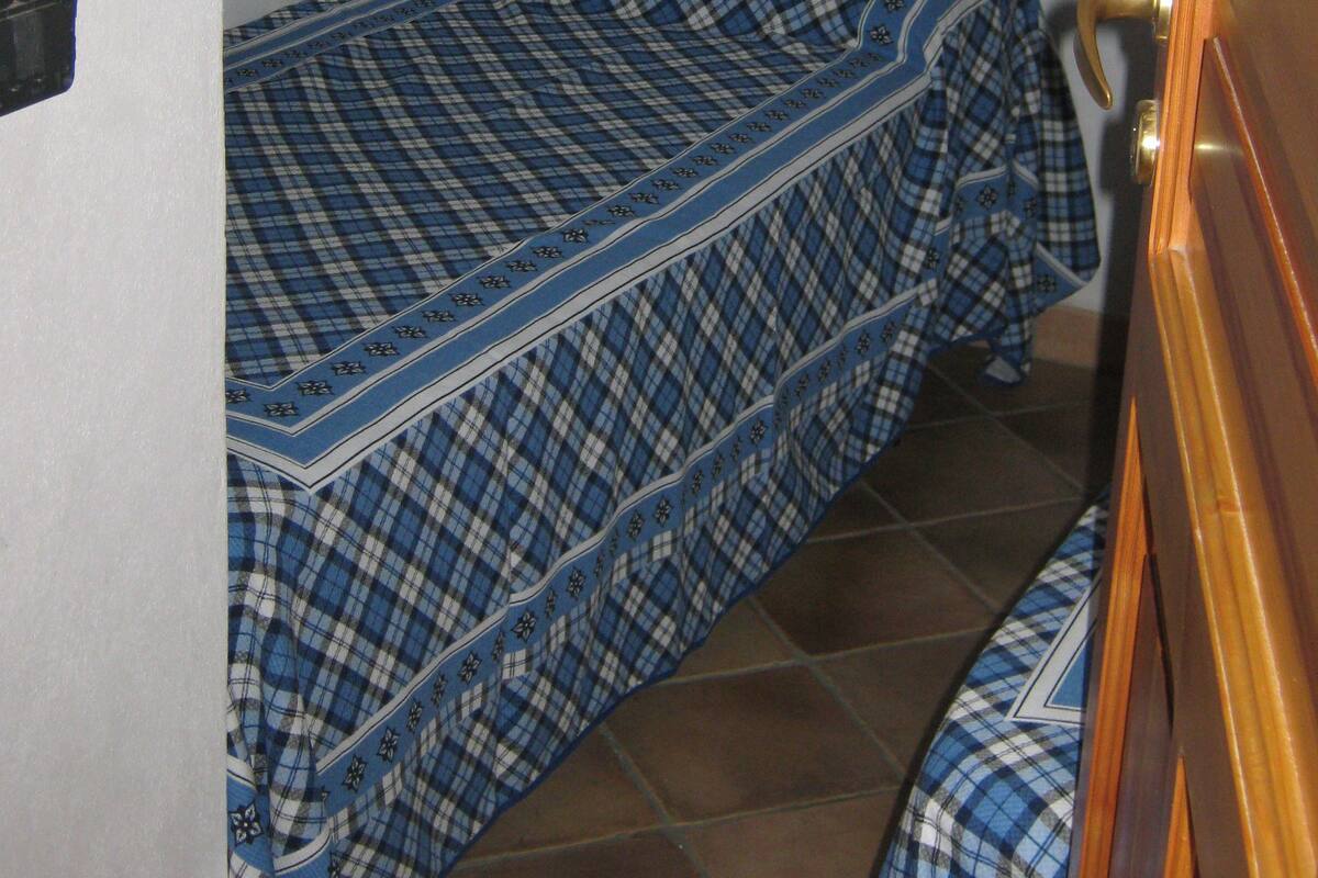 A bedroom with a bed covered in a blue and white checkered bedspread, a wooden nightstand, and a teddy bear on the wall.