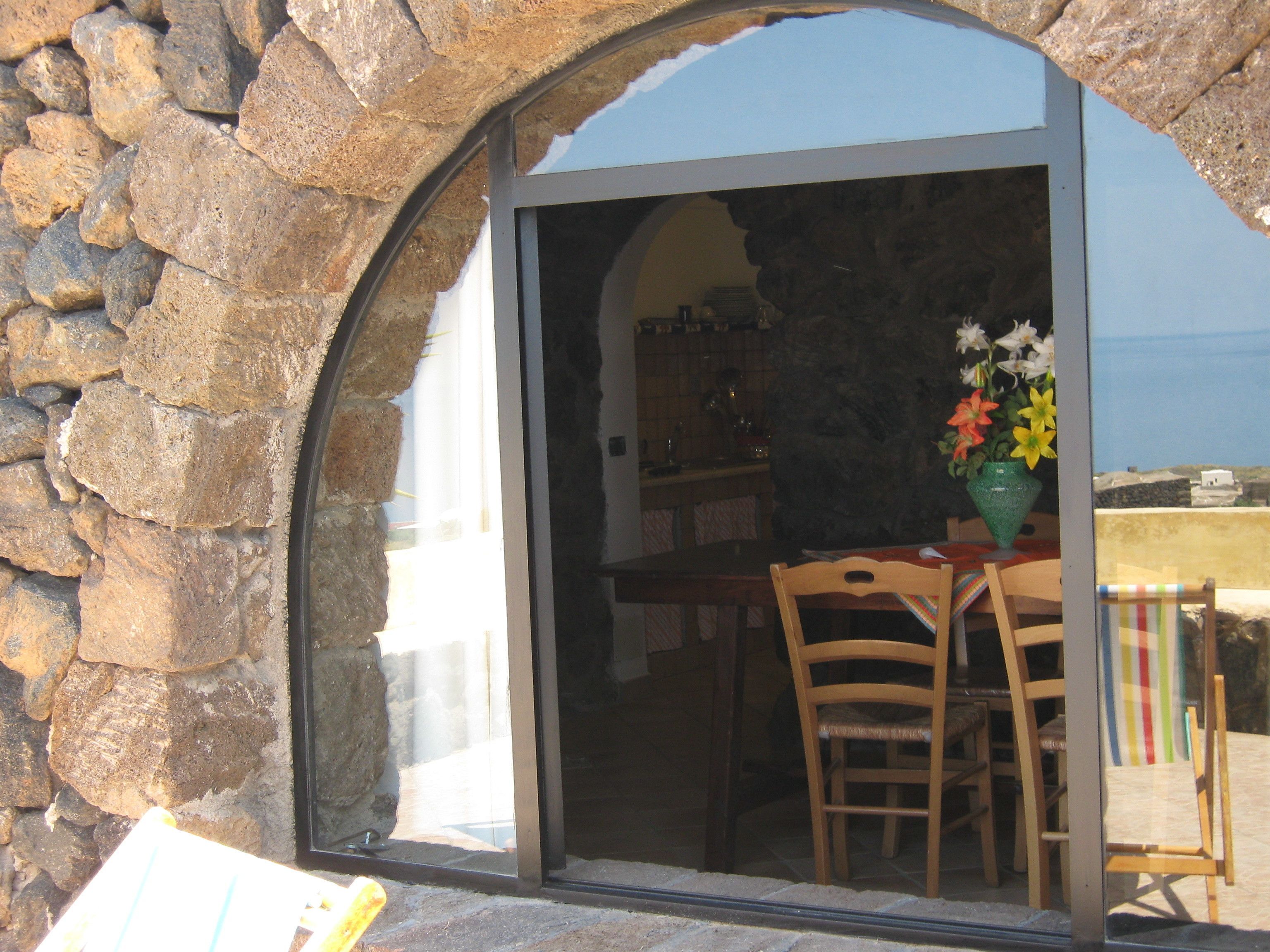 Un arco in pietra conduce a una sala da pranzo con tavolo, sedie e un vaso di fiori.