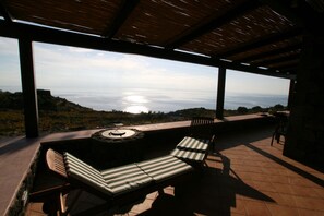 A covered outdoor seating area with a view of the ocean. - Agriturismo Zibibbodoro (Pantelleria)