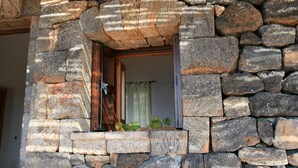 A stone wall with a wooden door and window, leading to a room with a curtain.