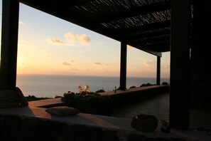 Une vue sur le coucher de soleil depuis un espace extérieur abrité, aménagé avec des sièges et une bouteille posée sur la table.