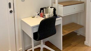 Un espacio de oficina compacto con un escritorio blanco, una silla de oficina negra, una cafetera y una estantería colgante.