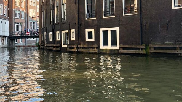 Un edificio a orillas de un canal, con fachada de ladrillo oscuro, varias ventanas y una pequeña torre.
